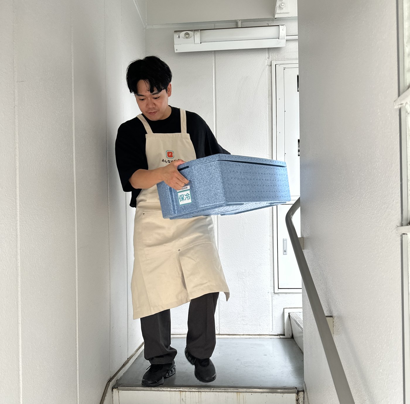 階段を降りて保冷BOXを運び出す配送パートナー