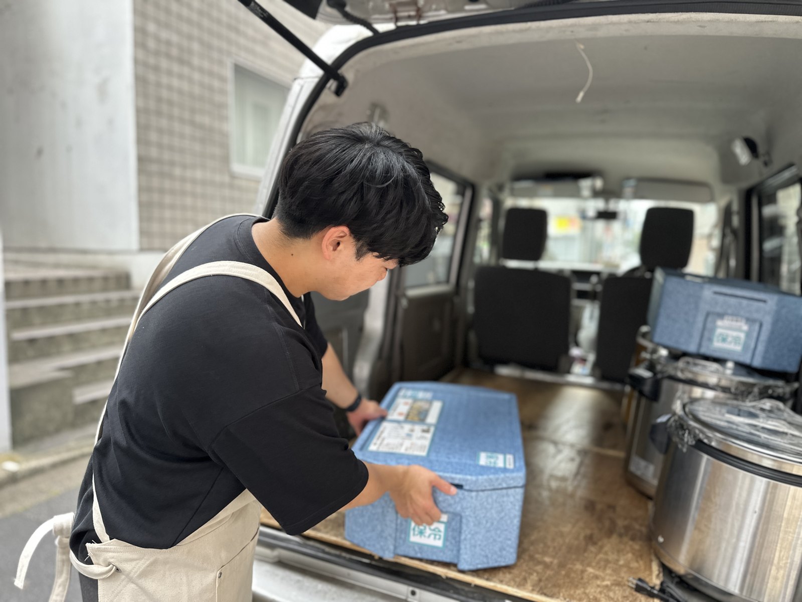 軽バンの荷台に保冷BOXとジャーを積み込む配送パートナー